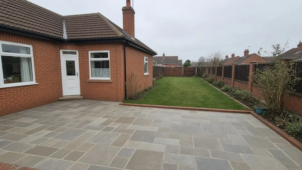 Example image: grey sandstone patio with a low brick edge behind a 1930s semi-detached house
